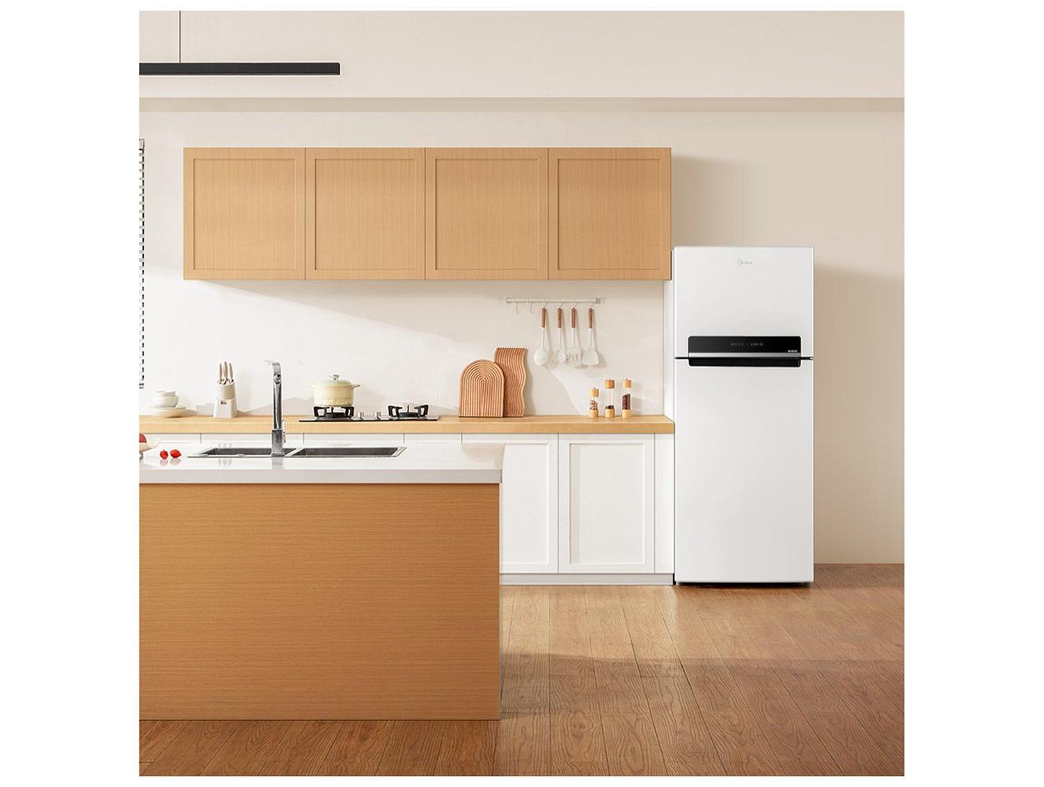 Geladeira Midea Frost Free Duplex branca posicionada em uma cozinha moderna ao lado de armários de madeira