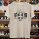 Camiseta Masculina NY Brooklyn Algodão Regular Fit Camisa Casual Urbana Manga Curta Personalizada Cor:Off WhiteTamanho: