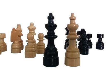 Antigo tabuleiro de xadrez de madeira com um conjunto de peças pretas e  brancas em uma posição caótica durante o jogo