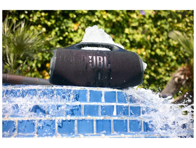 Caixa de som JBL Boombox 4 sobre uma borda de piscina com água espirrando ao redor