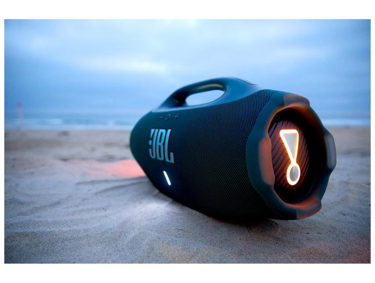 JBL Boombox 4 posicionada na areia de uma praia com o logo iluminado na lateral