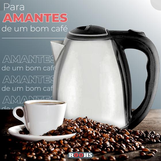 Chaleira elétrica de inox ao lado de uma xícara de café sobre uma mesa cheia de grãos de café