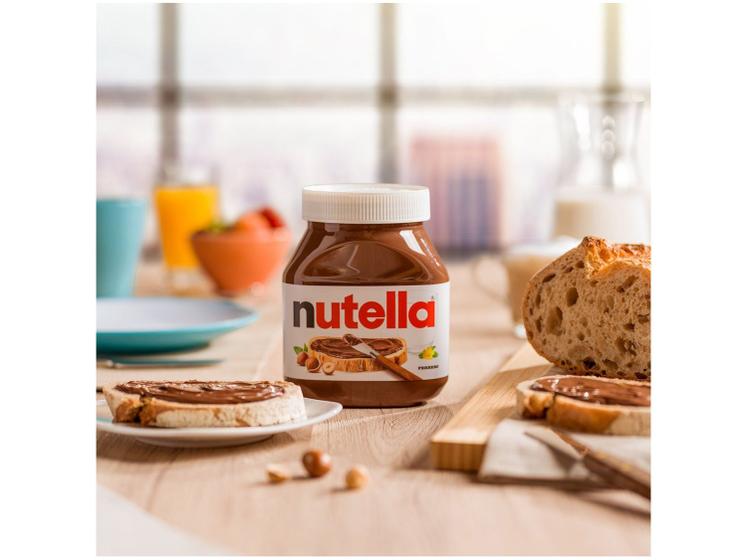 Pote de Nutella 650g em uma mesa de café da manhã com pães e suco ao fundo