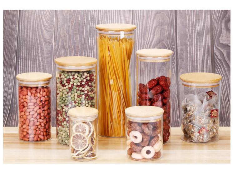 Vários potes de vidro Brinox Ekko, alguns cheios de alimentos como amendoim, ervilhas, macarrão espaguete, jujubas, tâmaras e chá, com tampas de bambu.