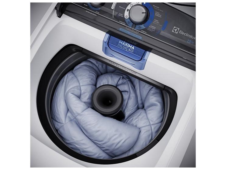 Vista superior interna da máquina de lavar Electrolux, mostrando um edredom azul claro dentro do cesto de inox e o dispenser de 'MÁXIMA DILUIÇÃO'.